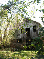 Digital photograph of a ramshackle barn as seen from photographer's mother's back yard, in a state of glorious decay framed by tree leaves in Webb City MO, © 2016 L. Eilee S. George